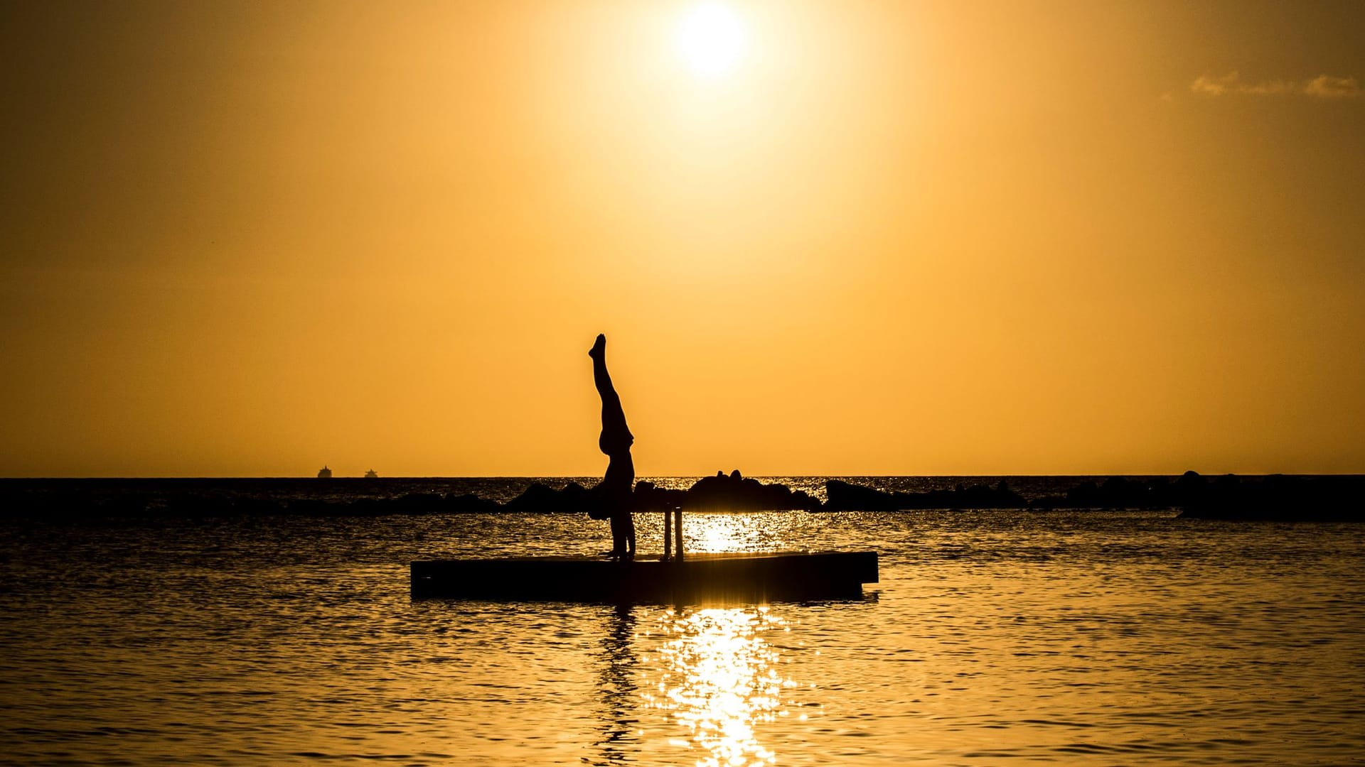 Silhouette of a handstand on a floating platform at sunset over the sea